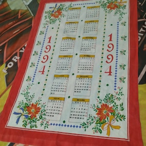 Puede incluir: Una toalla de cocina blanca con un borde rojo presenta un calendario para el año 1994. El calendario está dividido en 12 meses, cada uno con su propia cuadrícula de fechas. La toalla de cocina está decorada con diseños florales rojos y verdes.
