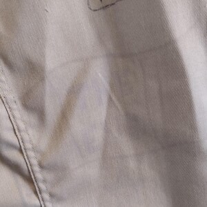 May include: A close-up of a light gray fabric with a subtle texture. The fabric has a seam running down the side.