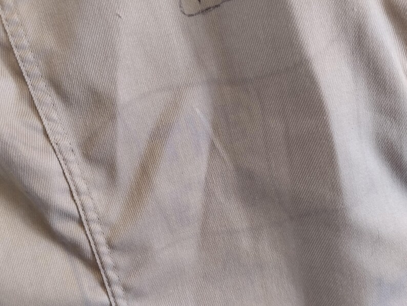 May include: A close-up of a light gray fabric with a subtle texture. The fabric has a seam running down the side.