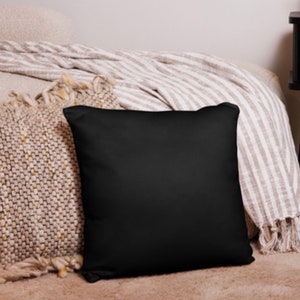 May include: A black throw pillow with a soft, smooth texture. The pillow is placed on a bed with a beige and white striped throw blanket.