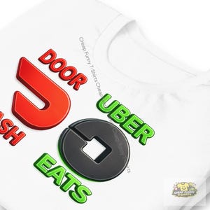 May include: White t-shirt with the words "DOOR DASH UBER EATS" in red, green, and black. The shirt has a crew neck and a small logo in the bottom right corner. The text "Cheap Funny T-Shirts Cheap" is also printed on the shirt.