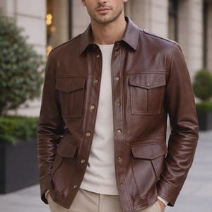 May include: A brown leather jacket with four front pockets and button closures. The jacket is worn over a cream-colored sweater and paired with khaki pants. The jacket has a collared neckline.