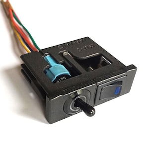May include: A black electrical switch panel with a toggle switch and a rocker switch. The toggle switch has a black lever, and the rocker switch has a blue indicator light. Wires of various colors extend from the panel. The word "Date" is visible on a blue connector.