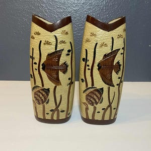May include: Two beige vases with brown fish and aquatic plant designs. The vases have a dark brown rim and base. The fish are brown with detailed scales. The vases are approximately 10 inches tall.