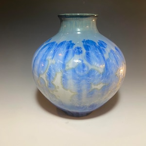 May include: A blue and white ceramic vase with a round body and a narrow neck. The vase has a unique, abstract design with swirling patterns and a glossy finish.