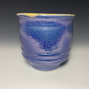 May include: A blue and purple ceramic mug with a slightly flared rim and a textured glaze.