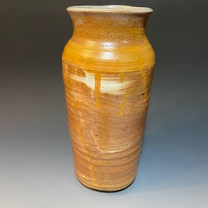 May include: A handcrafted ceramic vase with a warm, earthy color palette. The vase features a cylindrical body with a slightly flared rim. The exterior showcases a blend of brown and tan tones, with streaks of yellow and white, creating a textured, organic appearance.