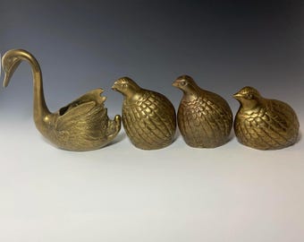 May include: Four brass animal figurines, including a swan, two quail, and a smaller bird. The swan is a planter with a hollowed-out body. The figurines are all in a gold tone.