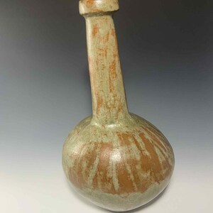 May include: A handcrafted ceramic vase with a bulbous base and a long, angled neck. The vase features a blend of earthy tones, including brown and green, with a textured surface. The vase is approximately 12 inches tall.