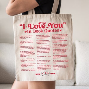 Könnte beinhalten: Eine weiße Einkaufstasche mit einem roten Aufdruck von Buchzitaten über die Liebe. Der Text lautet "I Love You" in Buchzitaten. Die Zitate stammen aus verschiedenen Büchern, darunter "Once Upon A Broken Heart", "Defy Me", "Twisted Hate", "All The Bright Places", "The Song Of Achilles", "Archer's Voice", "Say You Swear", "Love And Other Words", "The Fault In Our Stars", "A Court Of Wings And Ruin", "Throne Of Glass", "Beach Read", "The One", "A Kingdom Of Flesh And Fire", "The Queen Of Nothing", "Normal People", "The Last Olympian", "The Deal", "Fourth Wing", "Divine Rivals".