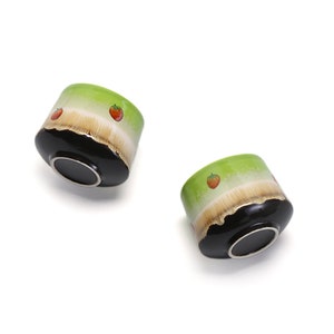 May include: Two green ceramic bowls with black rims and a white band. The bowls are decorated with small red strawberry designs.