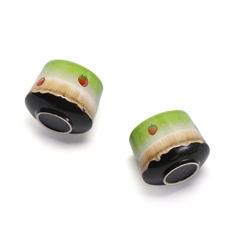 May include: Two green ceramic bowls with black rims and a white band. The bowls are decorated with small red strawberry designs.
