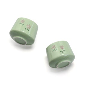 May include: Two green ceramic bowls with a floral design. The bowls have a white interior and a light green exterior with pink flowers and green leaves.