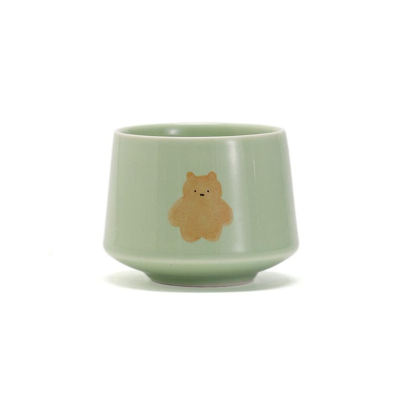 May include: A light green ceramic teacup with a brown bear illustration.