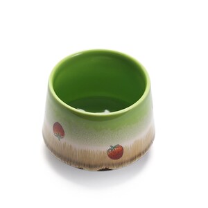 May include: A green ceramic bowl with a white and brown glaze. The bowl has a strawberry design on the side.