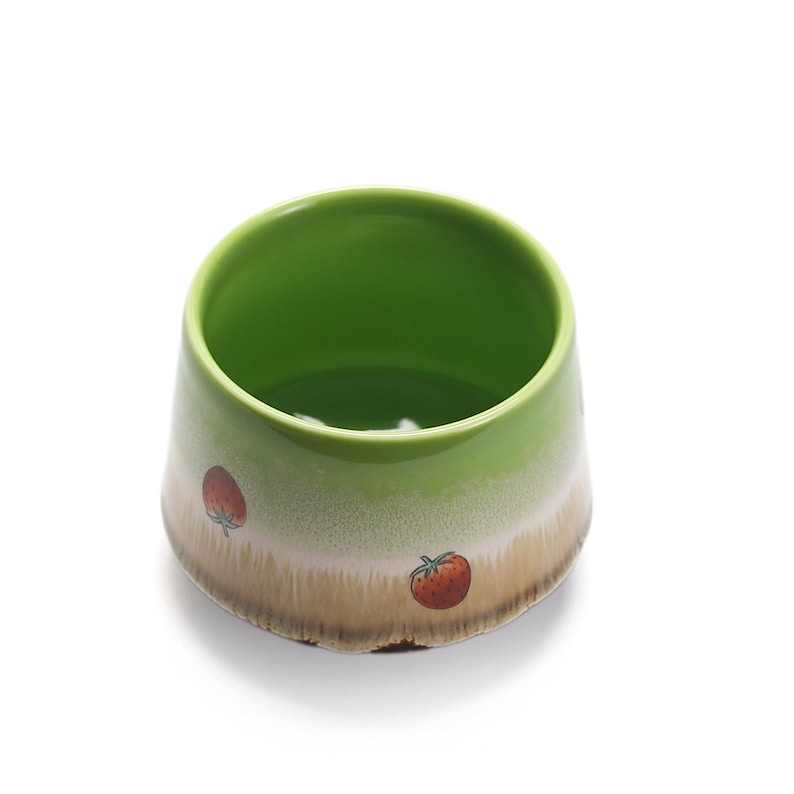 May include: A green ceramic bowl with a white and brown glaze. The bowl has a strawberry design on the side.