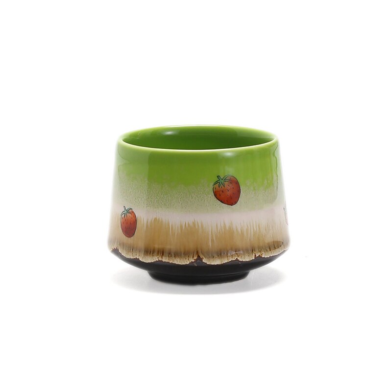 May include: A green ceramic teacup with a brown rim and a white band. The cup is decorated with red strawberries.