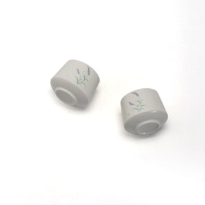 以下が含まれることがあります： 花柄の白いセラミック製のティーカップ2個。カップは薄いグレーの釉薬がかけられており、繊細なラベンダーの花柄が描かれています。