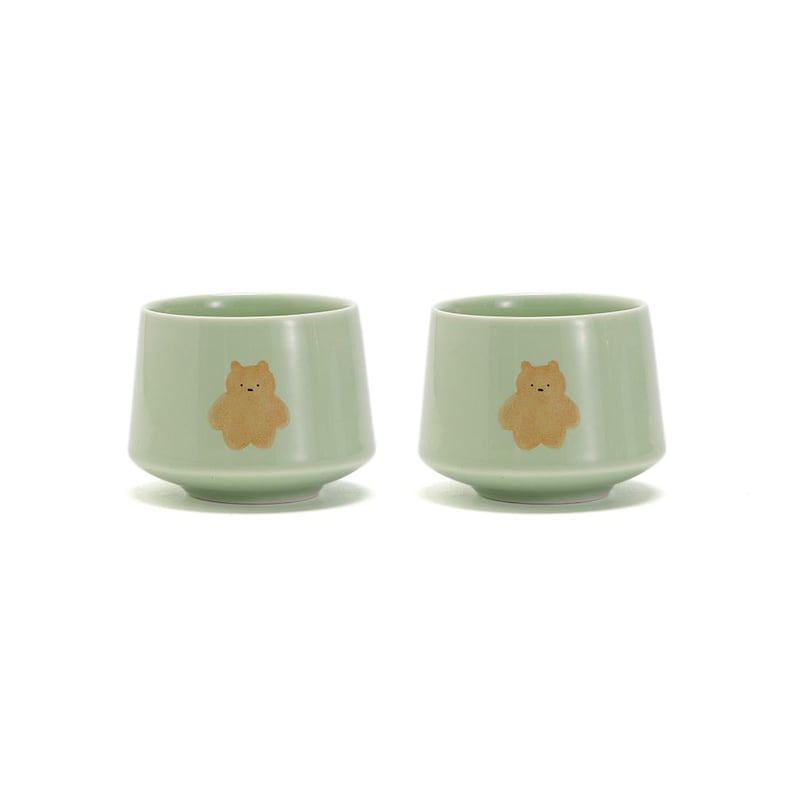 May include: Two light green ceramic teacups with a brown bear design. The cups have a rounded bottom and a slightly flared lip.