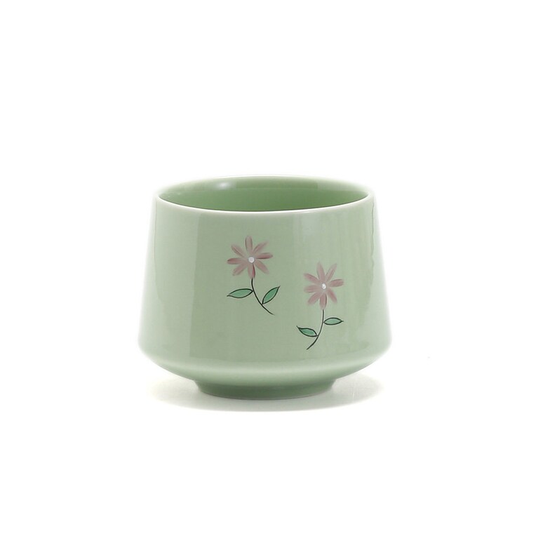 May include: A light green ceramic teacup with a floral design. The cup has two pink flowers with green stems and leaves.