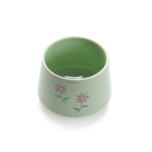 May include: A light green ceramic bowl with a floral design. The bowl has two pink flowers with green stems and leaves.