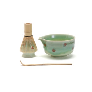 Puede incluir: Un tazón de matcha de cerámica verde con un diseño de fresa, un batidor de bambú y una cuchara de matcha de bambú.