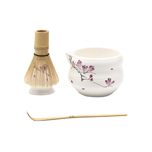 May include: A white ceramic matcha bowl with a floral design, a bamboo matcha whisk, and a bamboo matcha scoop.