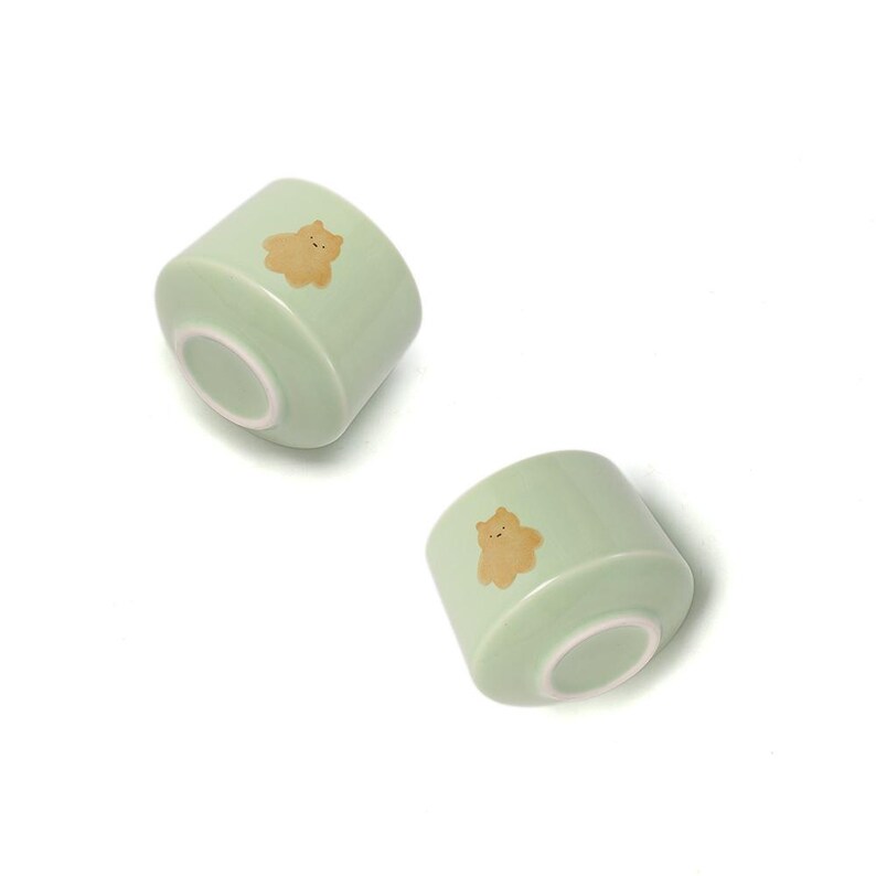 May include: Two light green ceramic bowls with a brown bear design. The bowls are turned upside down.