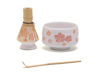 May include: A white ceramic matcha bowl with a floral design in shades of pink and orange. The bowl is accompanied by a bamboo matcha whisk and a bamboo matcha scoop.