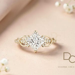 May include: A gold engagement ring with a large, square-cut, clear gemstone as the centerpiece. The ring features smaller accent stones and a delicate, swirling design on the band. The ring is set against a soft, neutral background.