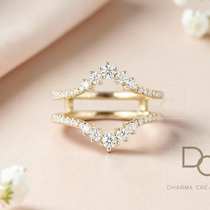 Puede incluir: Un protector de anillo dorado con un diseño de doble banda. Las bandas están adornadas con pequeñas piedras preciosas brillantes. El protector de anillo tiene un diseño en forma de V, con una fila de piedras preciosas más grandes en la parte superior e inferior de la V.