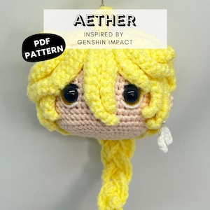 Pode incluir: Cabeça de boneca de crochê com cabelo amarelo em uma trança, olhos pretos e um rosto rosa claro. A boneca é inspirada em Genshin Impact e inclui o texto "AETHER" e "PDF PATTERN".