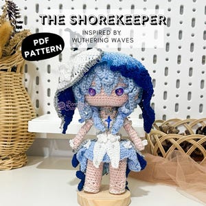 May include: A handmade crochet doll, "The Shorekeeper," inspired by "Wuthering Waves." The doll features a blue and white color scheme, with a detailed hat, dress, and hair. The doll is displayed on a wooden stand. The image includes the text "PDF PATTERN."