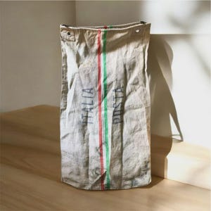 May include: A beige canvas bag with vertical red and green stripes down the center. The words "ITALIA POSTA" are printed vertically in faded blue. The bag has two metal eyelets at the top.