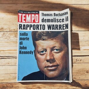 May include: A vintage Italian magazine cover featuring a portrait of John F. Kennedy with the headline "TEMPO demolisce il RAPPORTO WARREN sulla morte di John Kennedy." The magazine is set against a wooden background.