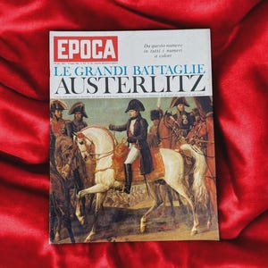 May include: A vintage magazine cover titled "EPOCA" with the headline "LE GRANDI BATTAGLIE AUSTERLITZ." The cover features a historical painting of Napoleon Bonaparte on horseback, surrounded by soldiers. The background is a deep red fabric.