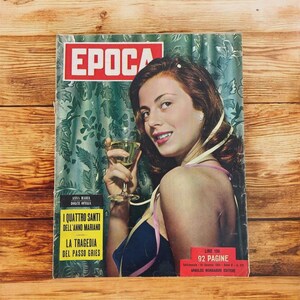 May include: Vintage magazine cover featuring a woman holding a glass of champagne. The magazine title is "EPOCA" in red letters. The cover includes text in Italian, with a green and white floral background.