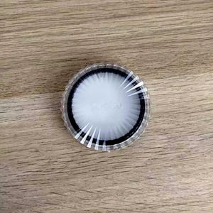 Puede incluir: Un objeto redondo y transparente con un centro blanco y un anillo negro. El borde exterior tiene un diseño estriado con líneas blancas que irradian desde el centro. Probablemente un filtro o un componente similar.