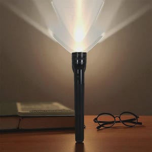 Könnte beinhalten: Eine schwarze Taschenlampe, die einen hellen Lichtstrahl aussendet und einen weiten Bereich beleuchtet. Die Taschenlampe ist zylindrisch und steht auf einer Holzoberfläche. Eine runde schwarze Brille und ein geschlossenes Buch befinden sich ebenfalls auf der Oberfläche.