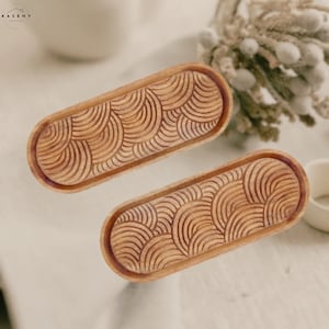 May include: Two wooden serving trays with an oval shape and a carved pattern of concentric circles. The trays are made of light brown wood and have a natural finish.