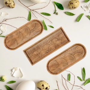 May include: Three wooden serving trays with a carved wave pattern. The trays are oval and rectangular in shape and are made of light brown wood.