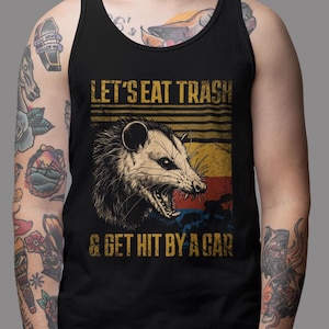May include: Black tank top with a vintage-style graphic of a possum with the text "Let's eat trash & get hit by a car".