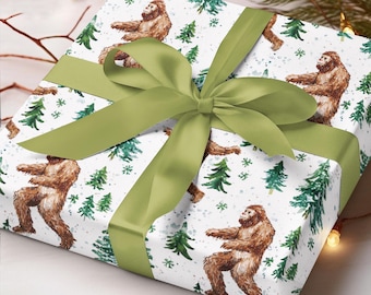 Puede incluir: Papel de regalo blanco con un patrón repetido de figuras marrones de Pie Grande caminando por un bosque nevado con pinos verdes. Una cinta de satén verde está atada en un lazo en la parte superior del papel de regalo.