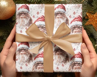 Puede incluir: Un papel de regalo blanco con un patrón repetido de un Bigfoot marrón y blanco que lleva un gorro de Papá Noel rojo. El regalo está envuelto con una cinta y un lazo marrones.