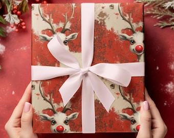 Op de afbeelding: Een cadeau verpakt in rood papier met een rendierenpatroon. Het cadeau is vastgebonden met een wit satijnen lint en strik. De rendieren hebben rode neuzen en geweien. Het thema is Kerstmis en cadeaus.