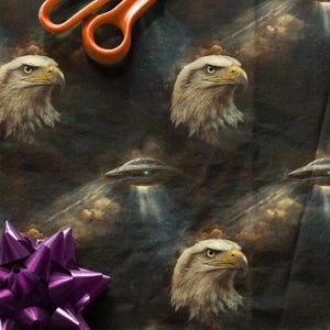 May include: Wrapping paper with a repeating pattern of bald eagles and UFOs against a dark, cloudy sky. A purple bow and orange scissors are in the image.