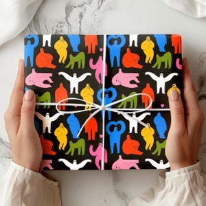 May include: A wrapped gift with a black background and a colorful pattern of abstract human figures in various poses. The figures are in shades of red, blue, yellow, green, pink, and white. The gift is tied with a white ribbon.
