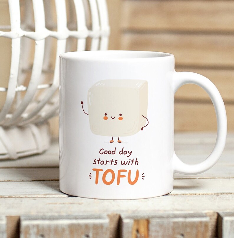 Może przedstawiać: Biały kubek ceramiczny z kresk&oacute;wkowym blokiem tofu z uśmiechającą się twarzą i tekstem "Good day starts with TOFU".