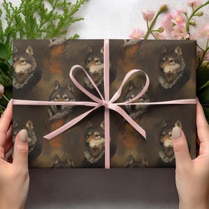 Op de afbeelding: Een ingepakt cadeau met een herhaald patroon van wolfportretten in kleding in renaissancestijl. Het papier is bruin met een roze lint dat in een strik is geknoopt. Groen en roze bloemen zijn op de achtergrond.