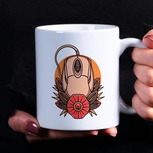 May include: White ceramic mug with a colorful illustration of a computer mouse with a red flower and green leaves. The mouse is brown and beige.